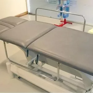 Barandillas de seguridad escamoteables instaladas en una camilla gris para tratamientos de fisioterapia